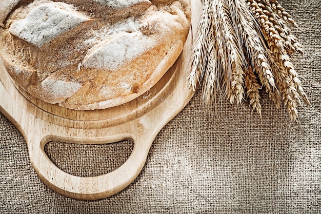 Chopping board bread rye ears on burlap background