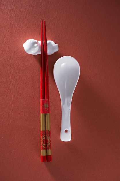 Chopsticks on chopstick rest and spoon against red background