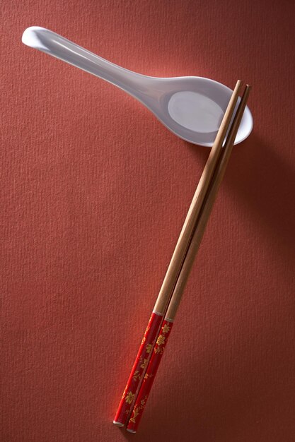 Chopsticks on chopstick rest and spoon against red background