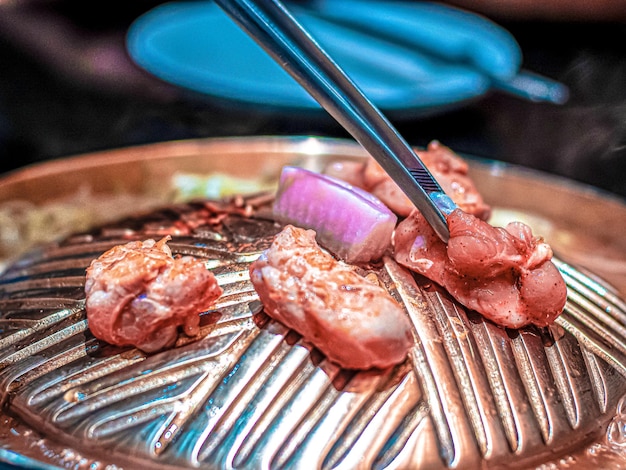 Foto bacchette che tengono carne o carne di maiale sulla padella calda