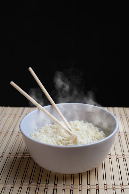 Chopsticks noodles with steam on black background asian noodle\
junk food concept