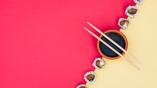 Photo chopsticks over the soya sauce bowl with sushi on yellow and red dual backdrop