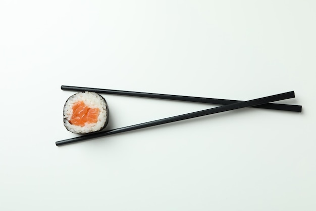 Chopsticks with maki on white background top view