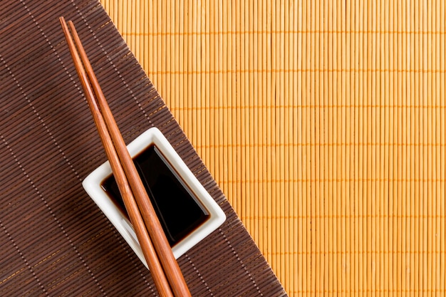 Chopsticks with soy sauce on two bamboo mat black and yellow top view with copy space