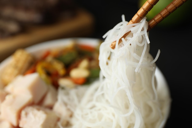 Фото chopsticks with tasty cooked rice noodles over bowl closeup space for text