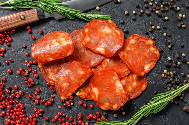 Chorizo sausage thin cut. Spanish salami with spices, paprika, pepper. Spicy food. Black background. Top view.