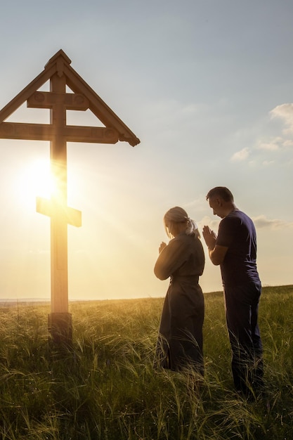 christelijk echtpaar bidt bij het kruis gebed tot God op de achtergrond van de zonsondergang hemel