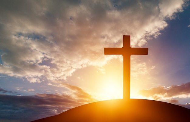 Christelijk houten kruis op de heuvel op zonsondergangachtergrond