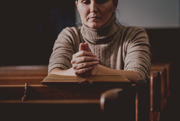 Christelijke vrouw bidden in de kerk. gekruiste handen en bijbel op houten bureau.