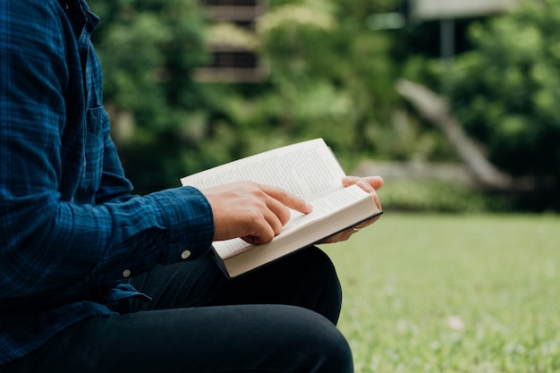 Christenen en Bijbelstudie concept. Jonge man zit het lezen van de Bijbel in de tuin. Kopie ruimte