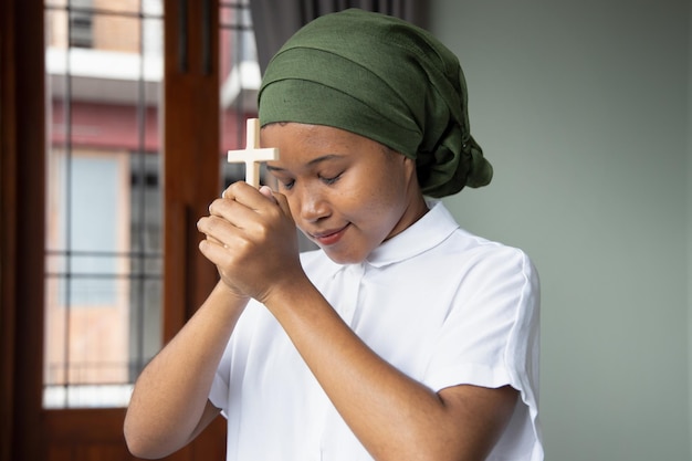 Christian African black woman cancer patient recovering from sickness praying to God with holy cross concept of cancer awareness related with Christianity