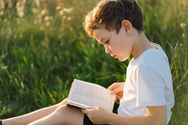 Il ragazzo cristiano tiene la bibbia nelle sue mani leggendo la sacra bibbia in un campo durante il bel tramonto concetto di fede, spiritualità e religione speranza di pace