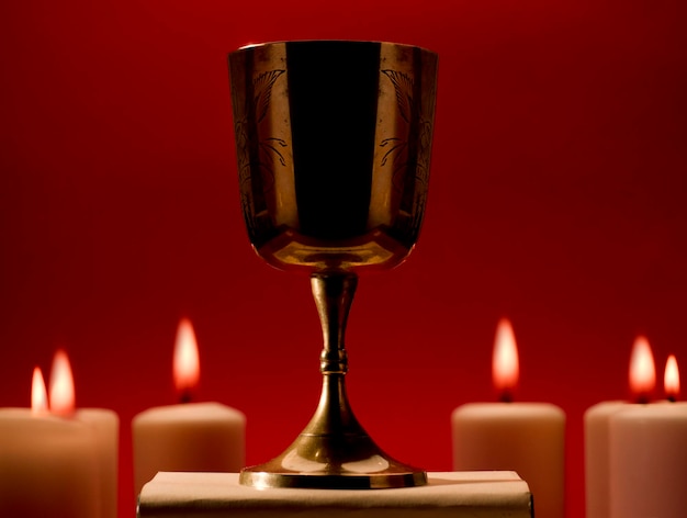 christian chalice on bible by burning candles red background