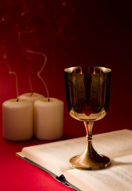 christian chalice on open bible with smoking candles and strong red background