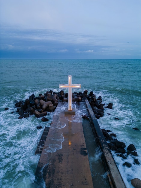 Christian cross standing on pier in the sea or ocean with dramatic sky at night