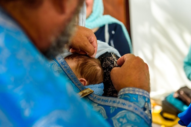 Христианский обряд крещения ребенка в церкви, священник помазывает мир ножкой маленького ребенка