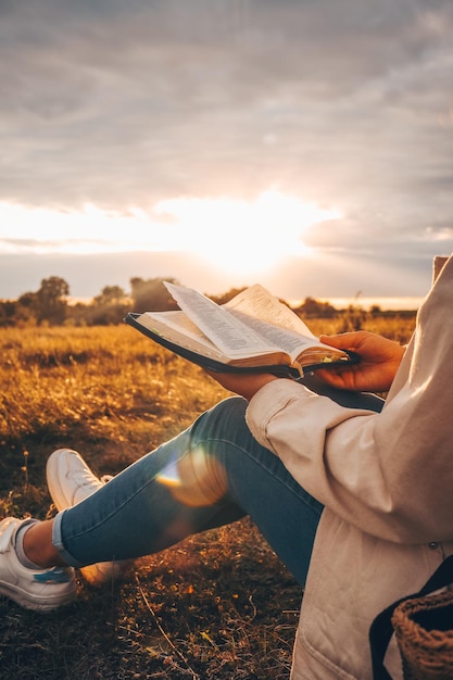 La donna cristiana tiene la bibbia nelle sue mani leggendo la sacra bibbia in un campo durante il bel tramonto concetto di fede, spiritualità e religione speranza di pace