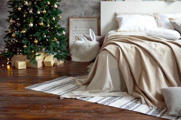 クリスマスアパートの装飾、スカンジナビアの居心地の良い家の装飾、クリスマスツリーの横にある暖かいニットブランケット付きのベッド。ライトと花輪。