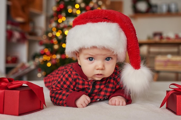 Рождественский мальчик в новогодней шапке на фоне елки с подарками.
