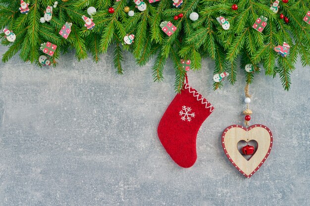 Christmas background. Christmas fir tree with red sock and wooden heart on gray 