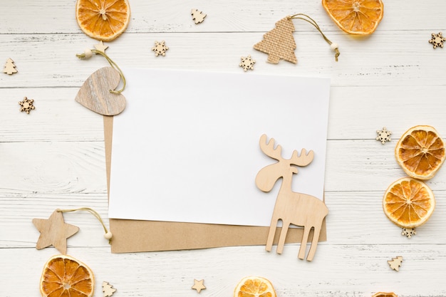 Christmas background from dried oranges, Christmas decorations and empty white card for greetings on a wooden table. Stars, hearts and Moose. Top view. Copyspace.