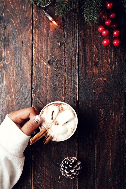 Christmas background - Girl hand holding cup of hot chocolate on wood table with rustic decoration and copy space, flat lay, top view. vintage color tone style.