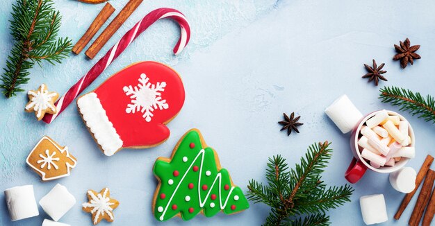 Christmas background. Group of gingerbreads, cinnamon, orange, toys and cup of hot chocolate on light blue background. Selective focus. Top view. Copy space