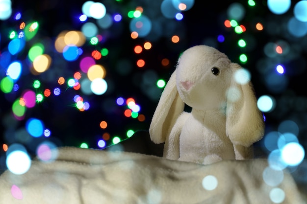 Christmas background. plush hare in the snow on a background of blurry lights.