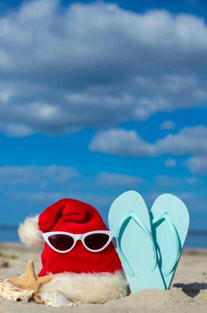 Foto sfondio natalizio cappello di babbo natale sulla spiaggia con stelle di mare e pantofole da spiaggia