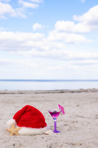 Christmas background Santa Claus hat on the beach with starfish and summer cocktail