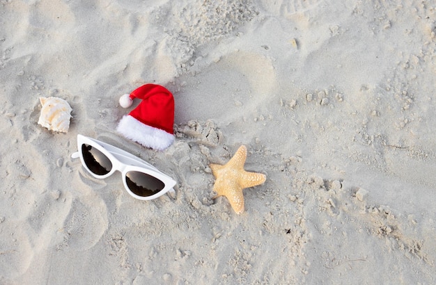 Sfondo di natale cappello di babbo natale sulla spiaggia con stelle marine e occhiali da sole