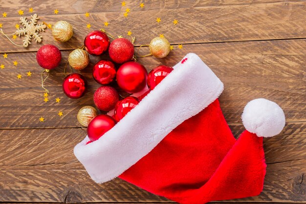 Christmas background. Santa Claus hat full of red and gold balls on wooden background.