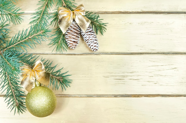 Christmas background, a spruce branch and two cones with a yellow bow and a yellow shiny ball with a bow on a gold wooden table