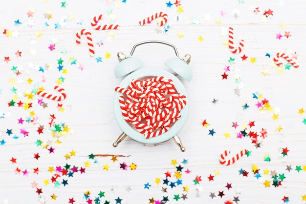 Christmas background with candy canes on alarm clock and multicolored sequins on wooden background