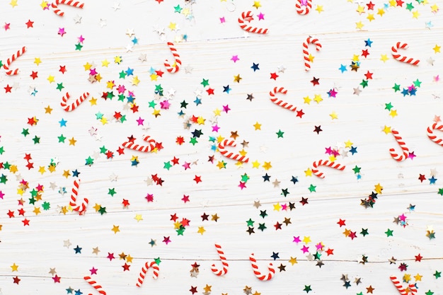 Christmas background with candy canes and multicolored sequins on blue wooden background