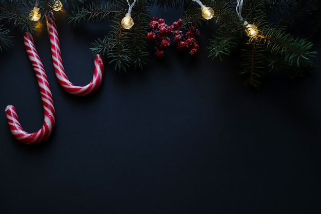 Christmas background with Christmas tree garland red berries and candy canes on dark texture