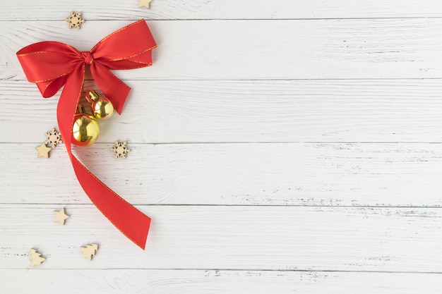 Фото Предпосылка рождества с декоративной композицией красного смычка и золотых шариков рождества на белой деревянной доске.