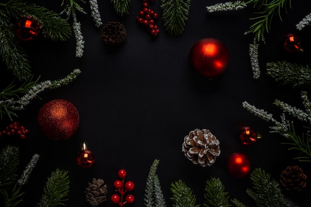 Christmas background with fir branches and red ball on dark and black background. Top view with copy space