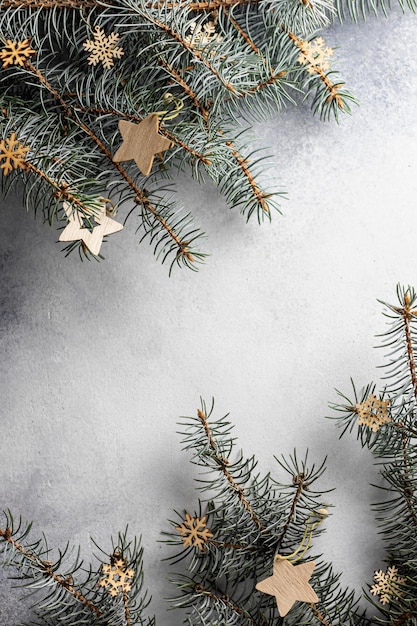 Christmas background with fir twigs with wooden stars and snowflakes on textured background with copy space. Top view. Vertical orientation