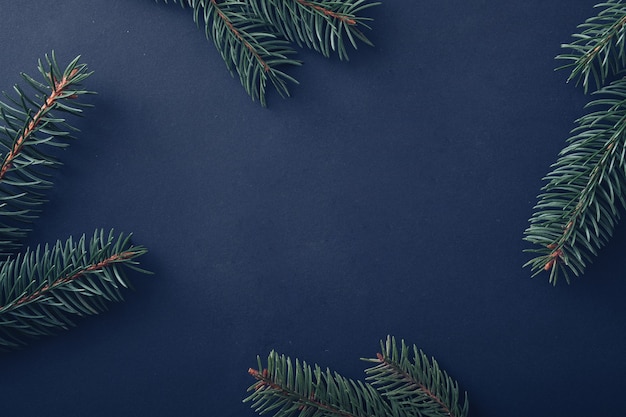 Christmas background with fresh pine branches arranged around the sides as a border on blue with central copyspace for holiday greetings