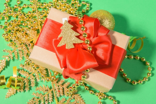 Новогодний фон с подарочной коробкой с красным бантом из ленты на праздничном золотом украшении на зеленом фоне.