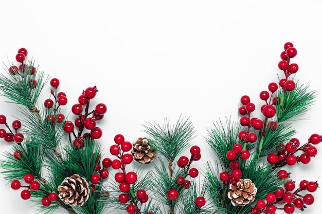 Christmas background with green fir tree branches, pine cones and red berries on a white backdrop.