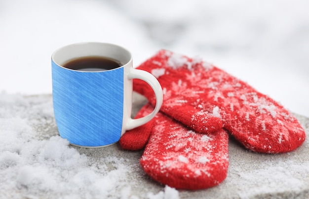 Christmas background with knitted red mittens and hot tea on a snowcovered park bench Selective focus