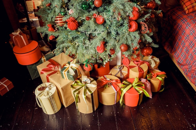 Foto sfondo natalizio con molte scatole regalo decorate con nastro sul pavimento sotto l'albero di natale vacanze invernali concept stack di scatole con regali sotto l'albero di natale