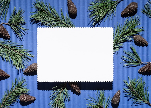 Christmas background with note paper on blue. Decor from pine branches and cones