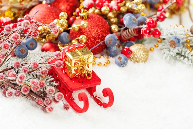 Фото Рождественский фон с красными санями санты и рождественским подарком на белом снегу с пустым местом для копирования