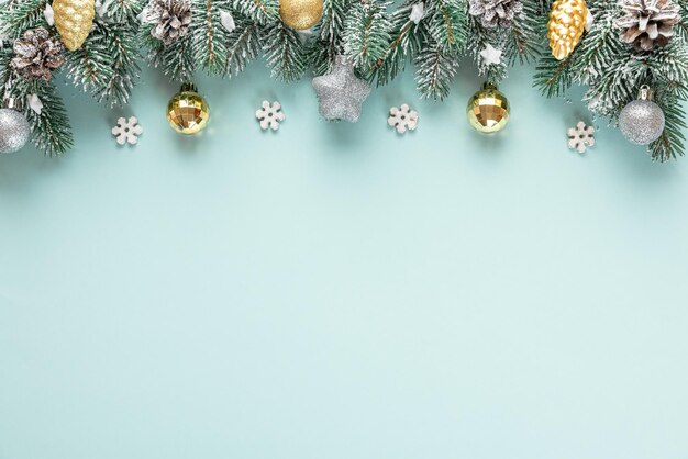 Christmas background with snowy fir tree with golden and silver decorations on blue background. Flat lay. Top view with copy space. Festive background