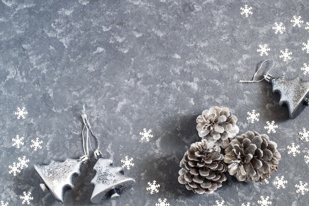 Новогодний фон со старинными серебряными елочными игрушками и шишками на серой бетонной поверхности