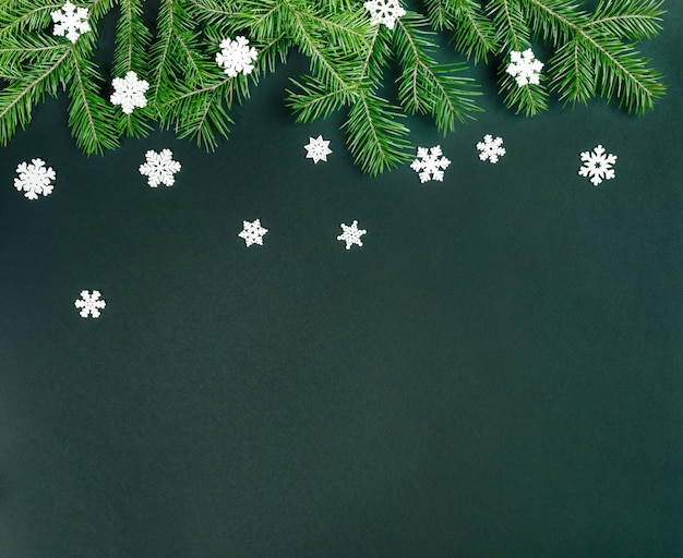 Christmas background with Xmas tree branches and white decorative snowflakes on green Copy space