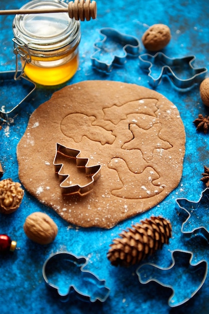 Christmas baking concept Gingerbread dough with different cutter shapes and spices on sides Top view on blue rustic background